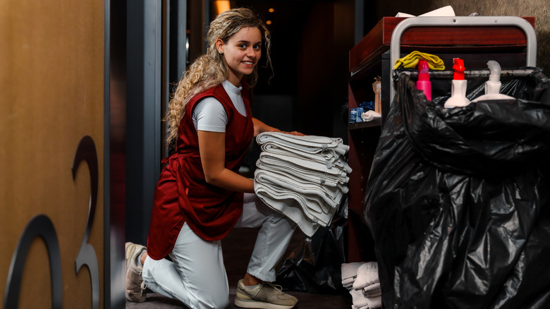 Young housekeeper holding towels next to housekeeping cart