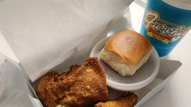 A to-go box of chicken with a pickle, bun, and drink from Frenchy's Chicken.