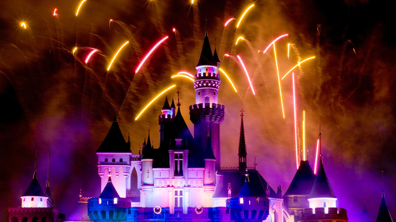 Fireworks in the sky against a colorfully lit theme park castle
