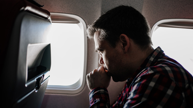 A man in a shirt looking anxious out of an airplane window
