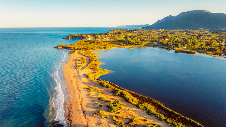 Halikounas Beach Corfu sand lit by golden sun with waves crashing on shore and still lake