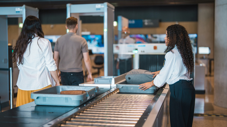 Airport passengers entering a metal detector as a TSA agent looks on