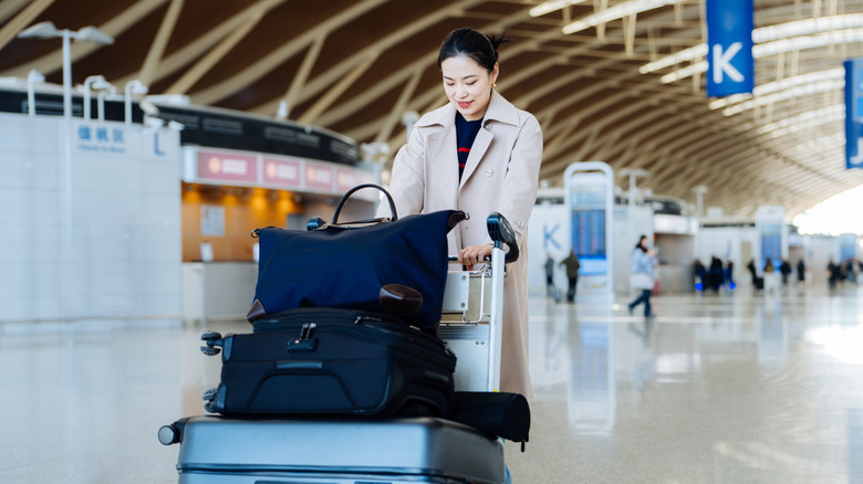 Woman in an airport pushing a cart with stacked bags