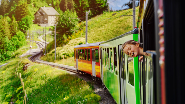 Little girl pokes her head out of train in Alpine scenery in Switzerland