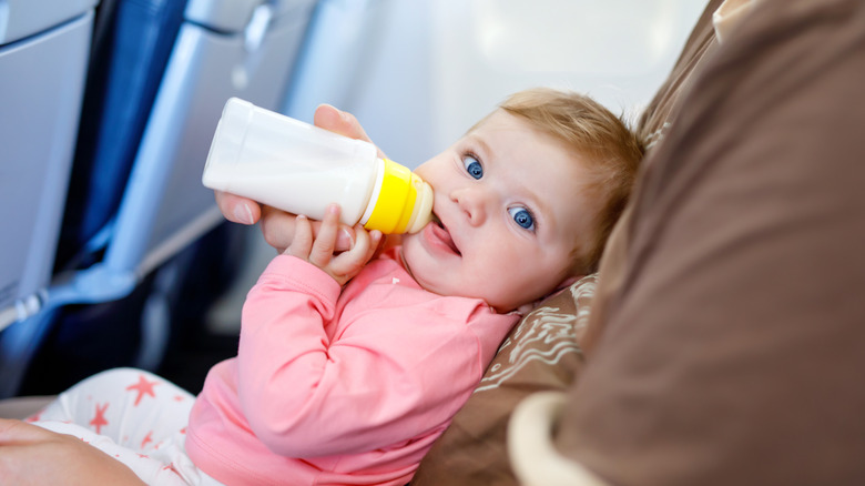 A happy baby drinks from a bottle on a flight