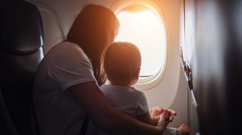 A parent holding a baby on her lap look out the plane window at the sunset