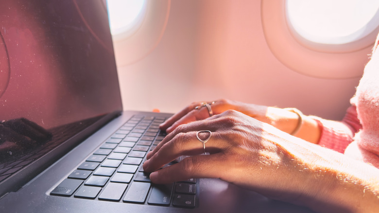 Person in a window seat on a plane, typing on a computer