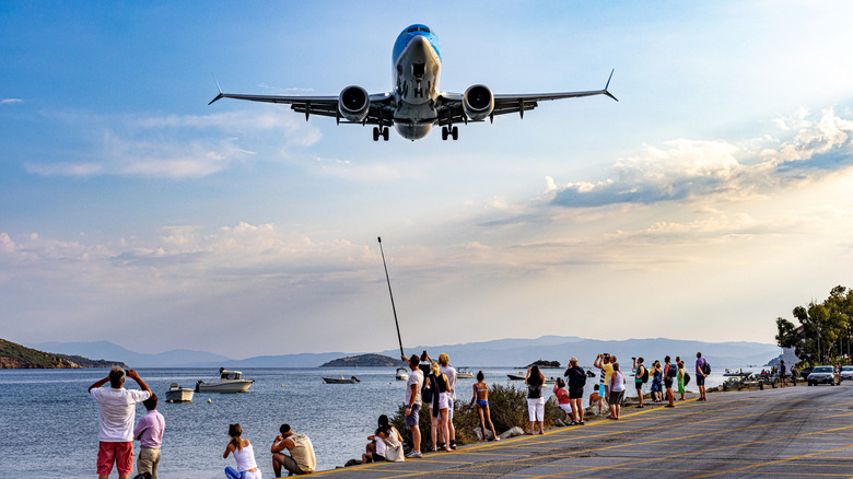 Plane flying over tourists as it lands at Skiathos in Greece.