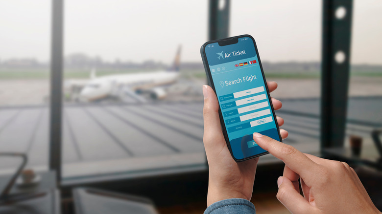 User holding a smartphone and booking cheap flights online, airport in the background