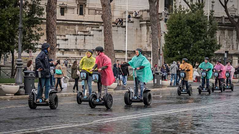 View of tourists in wet weather ponchos riding Segway around Rome.