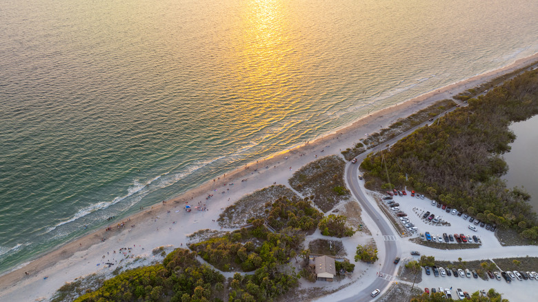 An aerial view of Blind Pass Beach in Florida, with clean white sand and water, people, cars, and trees