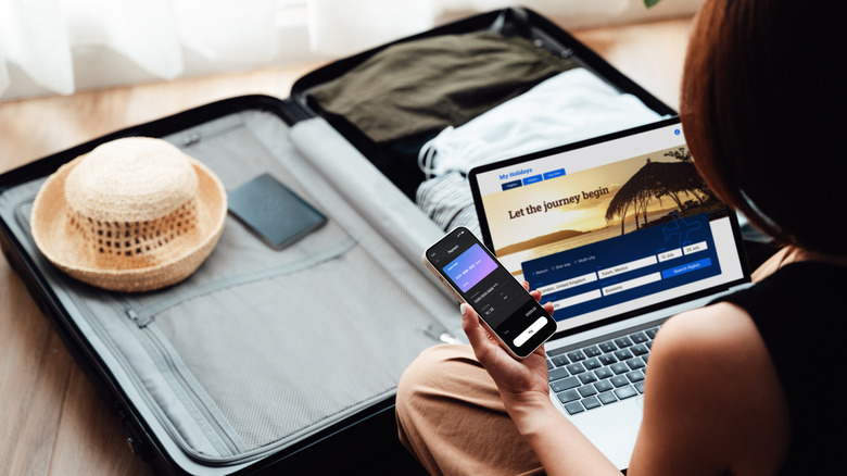 Traveler with suitcase checking laptop and mobile phone