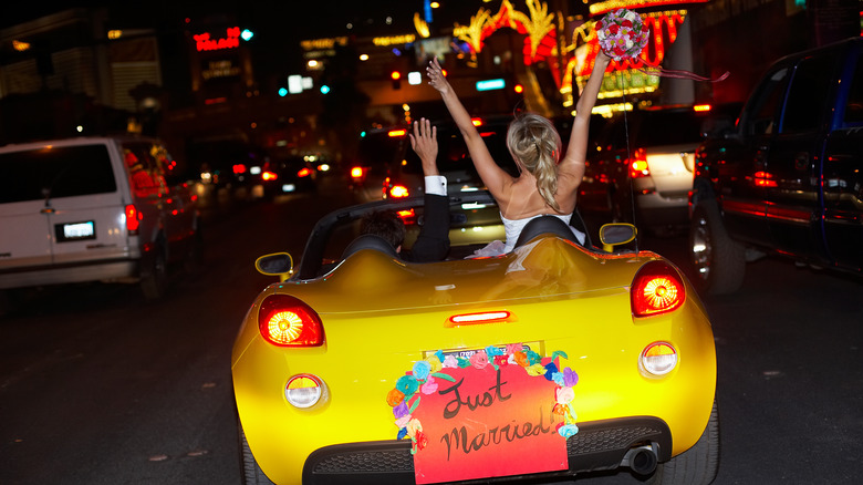 Bride and groom in Vegas, celebrating in a yellow sports car that says "just married"