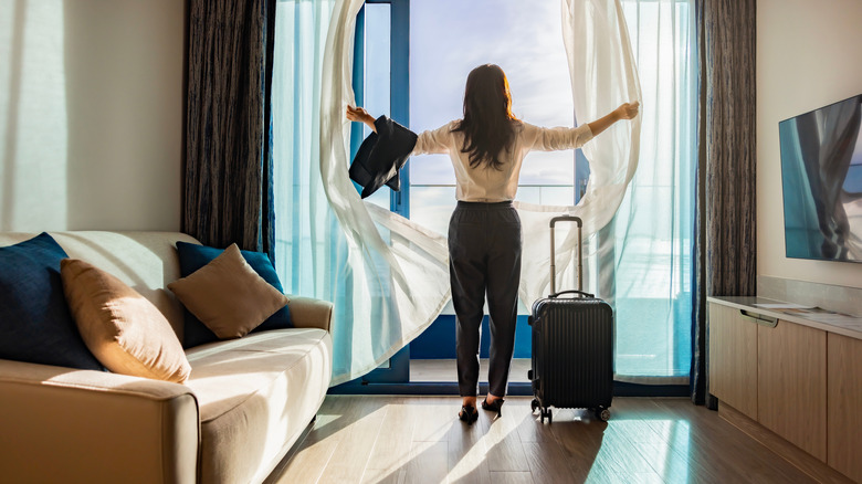 Woman opening curtains in hotel room