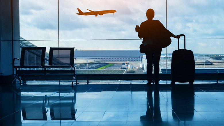 Silhouette of a woman with luggage watching a plane take off