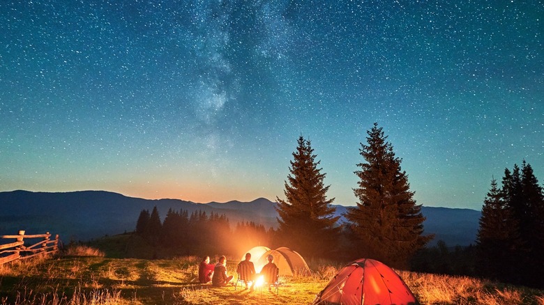 People camping around a fire with tents and a starry sky