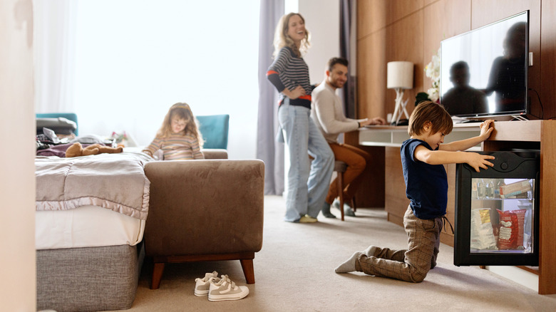 A boy opening a hotel minibar fridge while his parents watch and smile