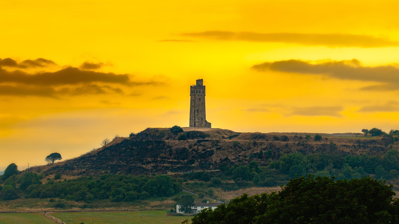 Tower atop mound hill in the countryside against orange sky