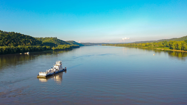 A boat drifts down the Ohio River, flanked by banks lined with trees