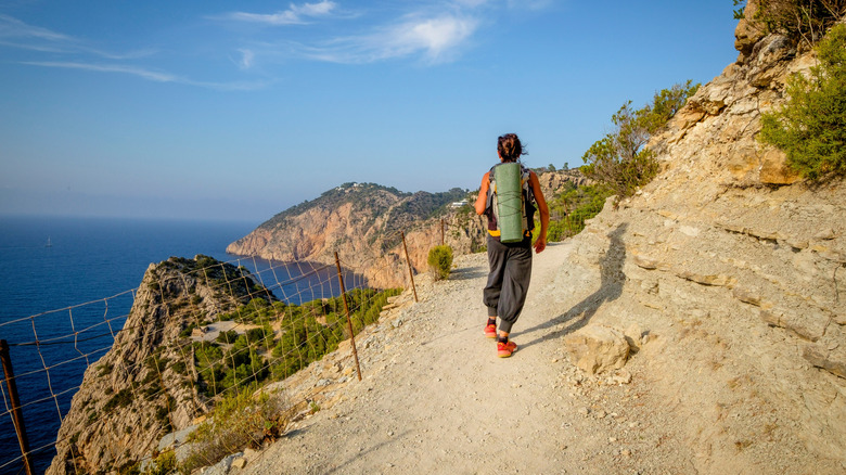 Hiker with backpack walking along a cliffside path with ocean view