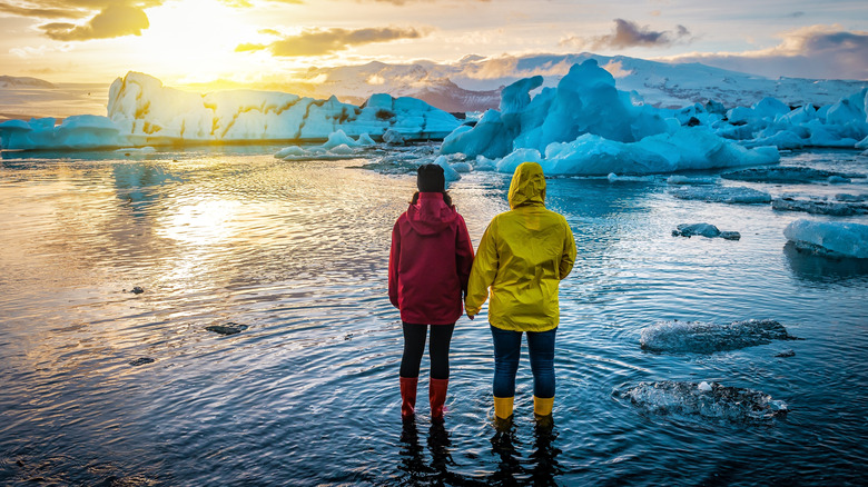 Two people watch as the sun sets over a glacier lagoon in Iceland
