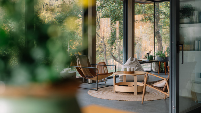 Two low chairs and a beanbag in a minimalist living room with floor-to-ceiling windows and views of the woods.