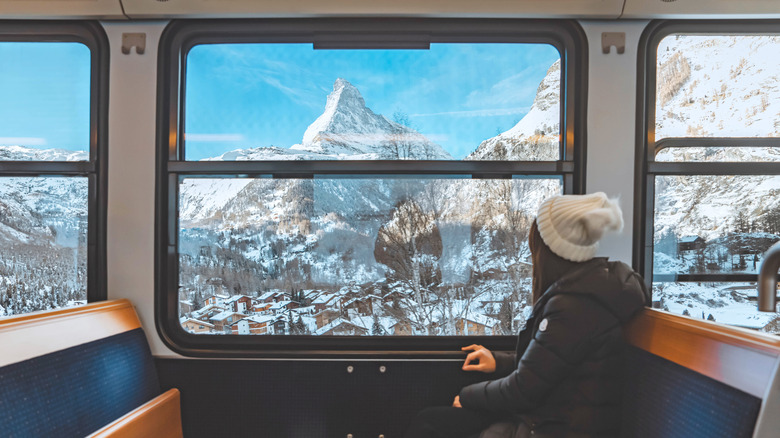 A woman looking out of a train at a snowy Swiss landscape.