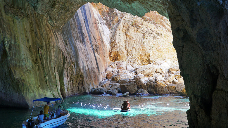 Boats passing underneath an arched cliffside formation.
