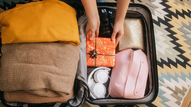 Person packing suitcase and putting wrapped gift inside