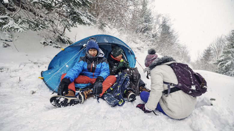 Three happy teenagers camping in the snow with a winter tent.