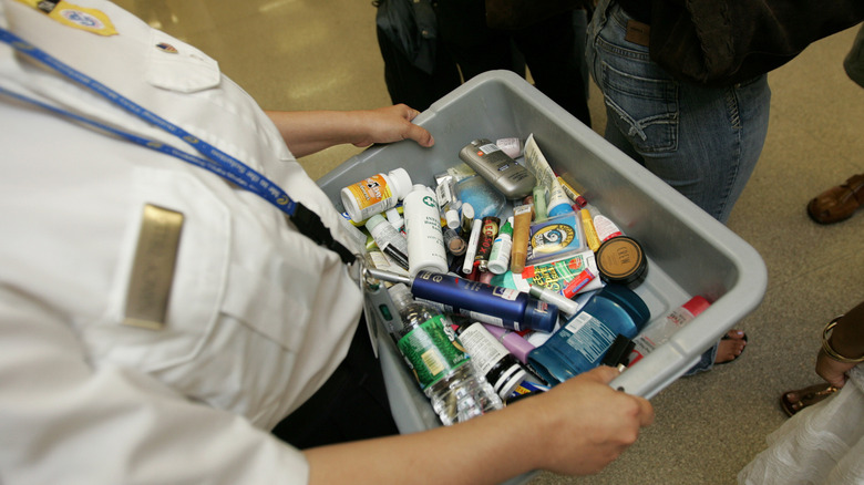 A TSA agent carries a bin full of confiscated liquids