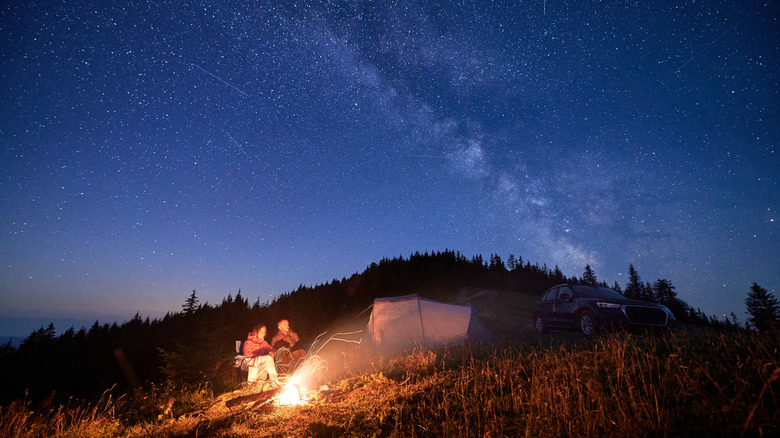 A couple camp next to a fire under a starry sky