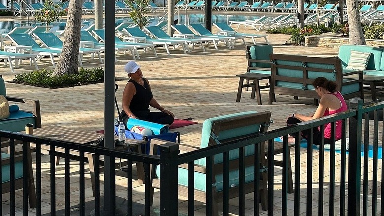 two people sitting on yoga mats with pool chairs around them