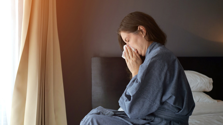 a woman blows her nose in a hotel room.