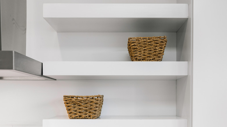 white floating shelves next to a kitchen hood with baskets on top