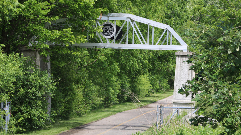 A sign for the Cal-Sag Trail over a walking and cycling pathway bordered by lush greenery.