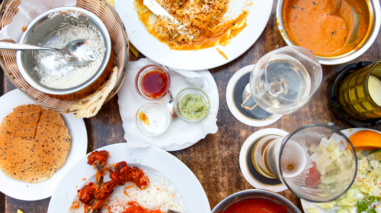 A top-down view of a wooden restaurant table piled with glasses, plates, and bowls of half-eaten food