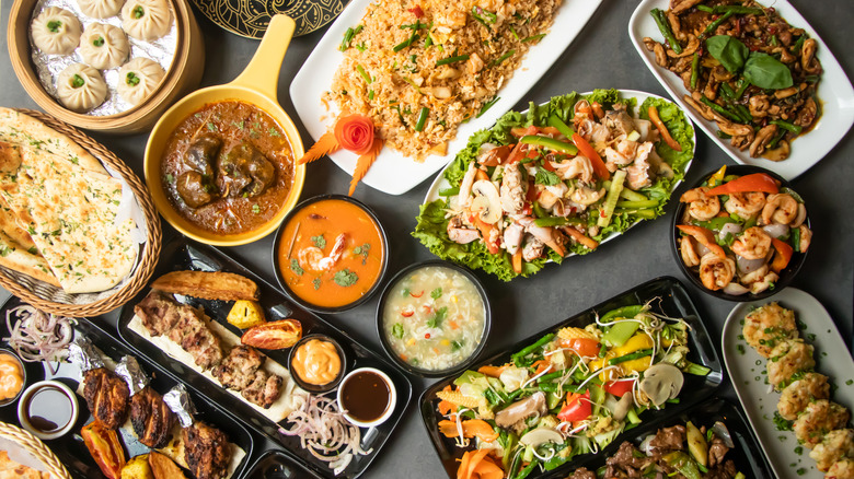 Top-down view of a wide variety of south Indian dishes on a table, including mutton masala, chicken karahi, garlic naan, and more