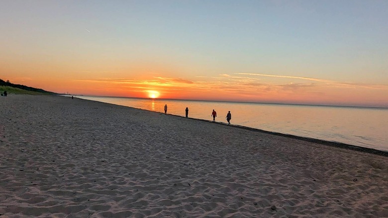 Silhouettes of four people walking along wide sandy Kemil Beach as sun sets over Lake Michigan in the background