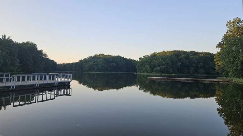 Still water on a lake, with a dock and trees around it, at Shakamak State Park