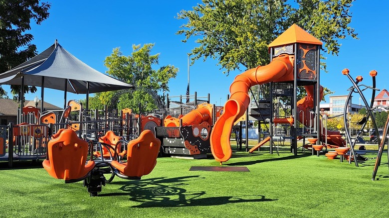 An orange playground at Arch Street Park in Lawrenceburg Indiana, with curvy slides, chairs on springs, and more