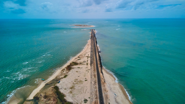 Top view of a long strip of road on a blue green sea, with sandy beaches along both sides