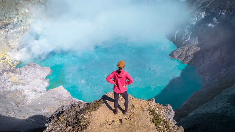 A women in a red jacket stands at the crater rim of Mount Ijen in Indonesia.