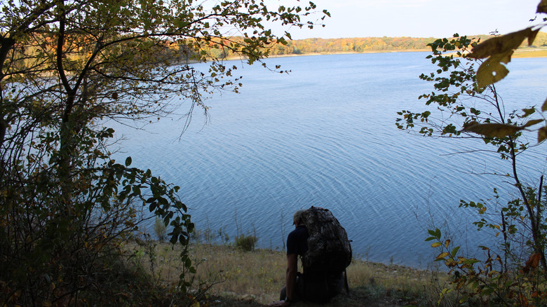 A hiker with a backpack sitting on the shoreline of Coralville Lake at Sugar Bottom Recreation Reserve.