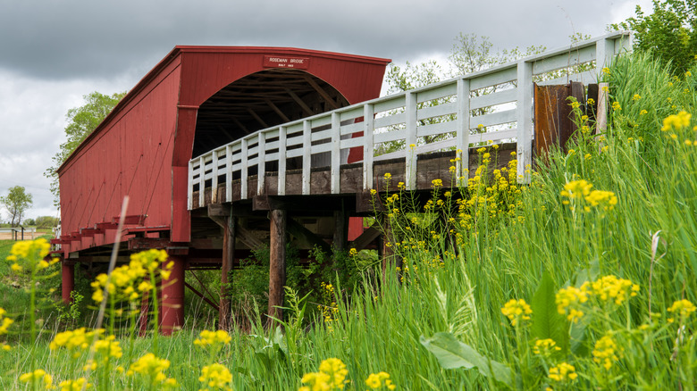 Roseman Covered Bridge in Winterset, Iowa, surrounded by flowers on a cloudy day