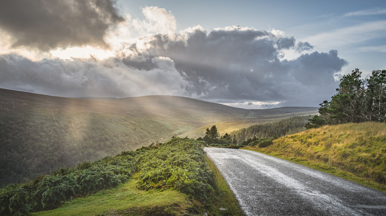 Winding road leading to Lough Tay, aka Guinness Lake, illuminated by rays, Wicklow Mountains, Ireland