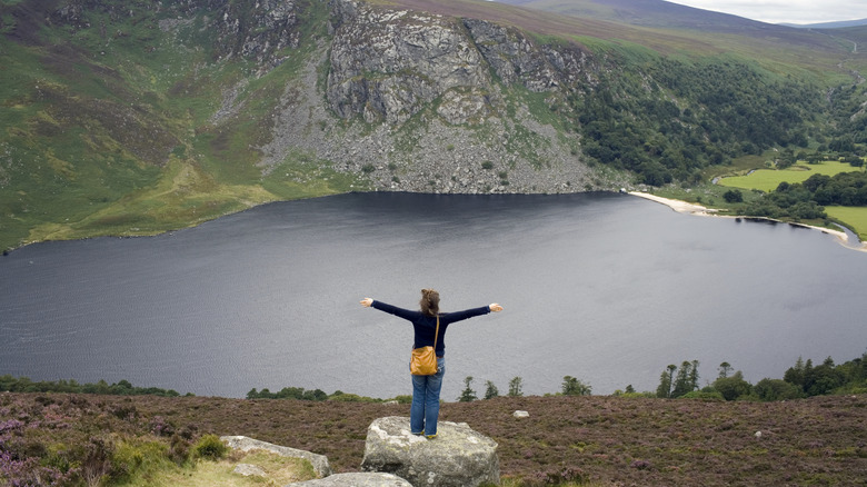 A woman spreading their arms with Lough Tay, aka Guinness Lake, in the background, Wicklow Mountains, Ireland