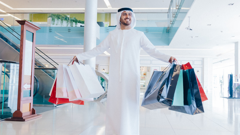 A man dressed in a thawb holds bundles of shopping bags