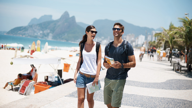 A couple walking on the beach holding a map and guidebook