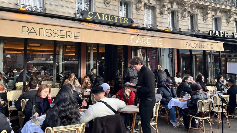 Customers sitting outdoors under yellow awning of Carette café in Paris